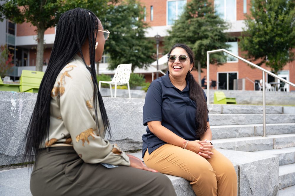 two women sit on a stone bench facing each other