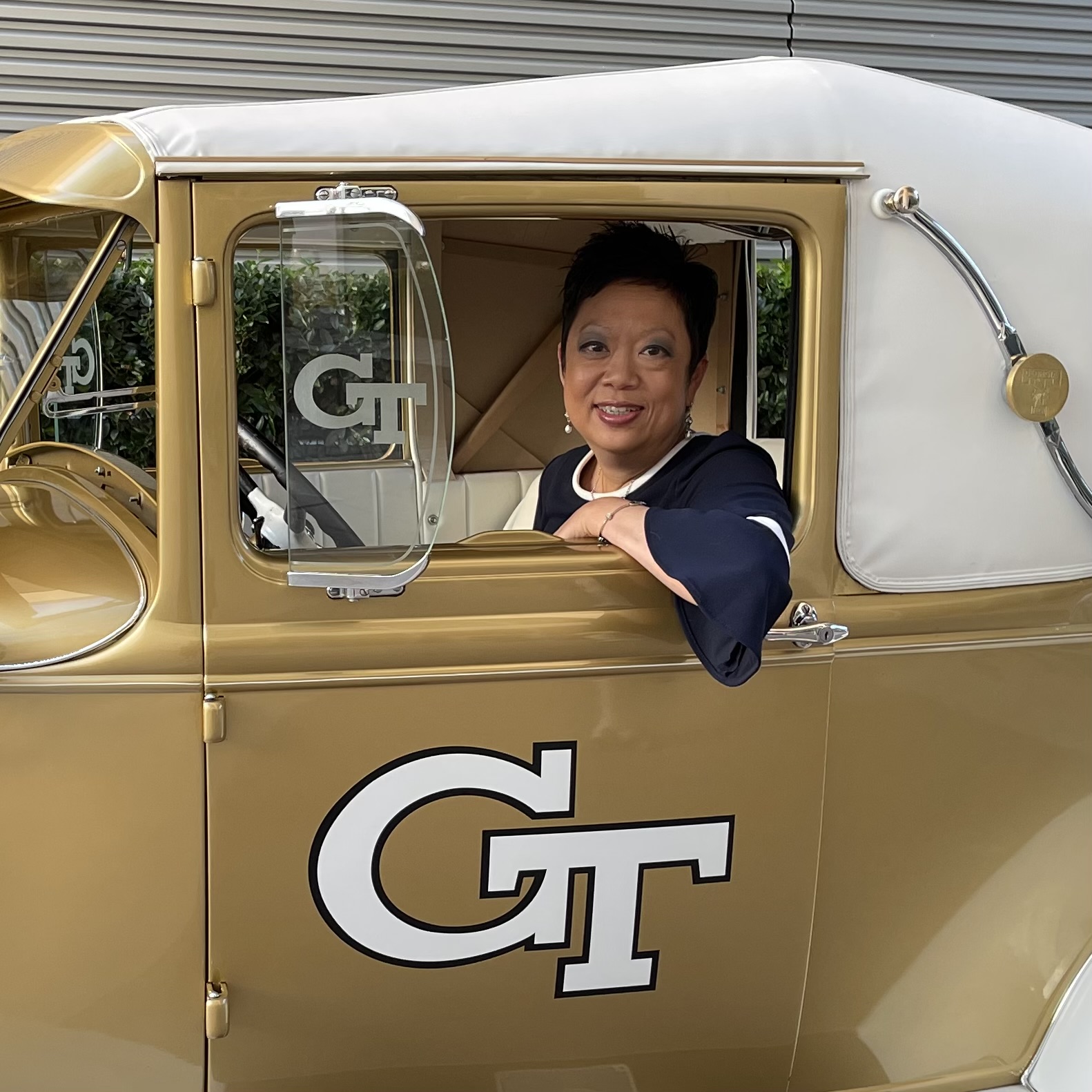 A woman sits in the driver's seat of a gold convertable Model T car