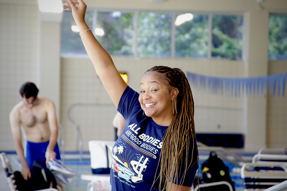 A smiling woman stands with one hand raised