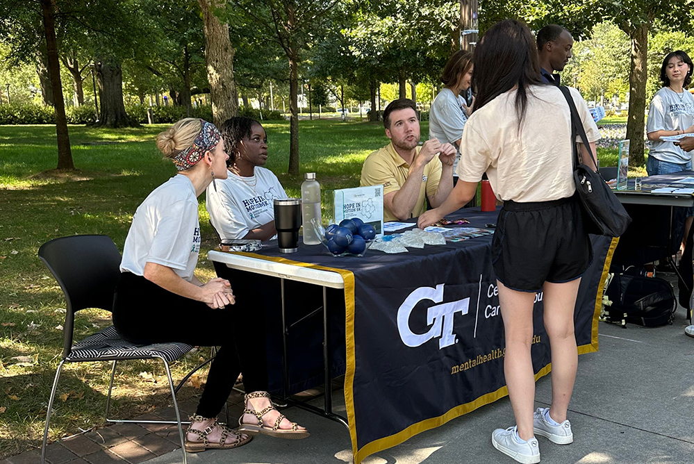 People sit outdoors behind a table talking to a visitor
