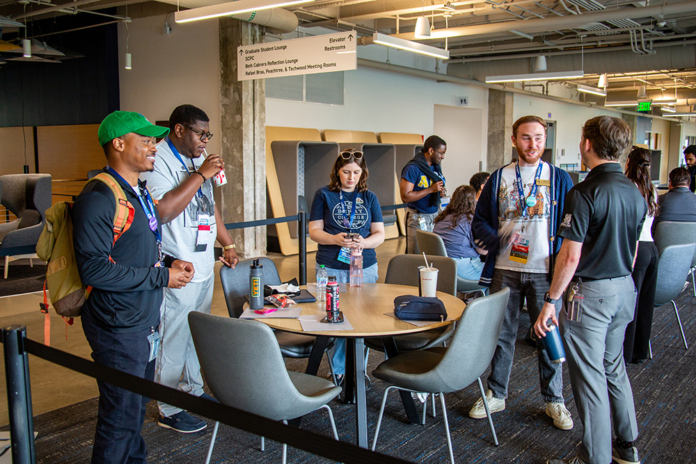 People engaged in conversation stand and sit at a table